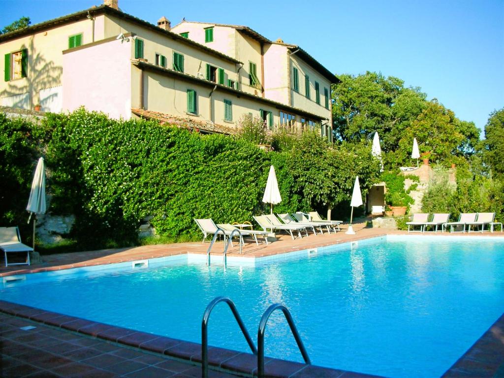 卡斯特利纳-因基安蒂卡萨莱奇酒店的一座带椅子和遮阳伞的游泳池位于一座建筑旁边