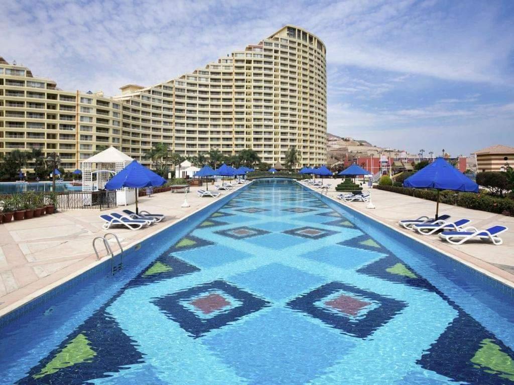 艾因苏赫纳Porto Sokhna的一个带椅子和蓝伞的游泳池以及酒店