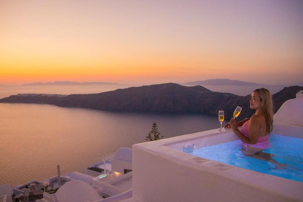 易莫洛林Esmi Suites Santorini的坐在游泳池边的女人,喝一杯酒