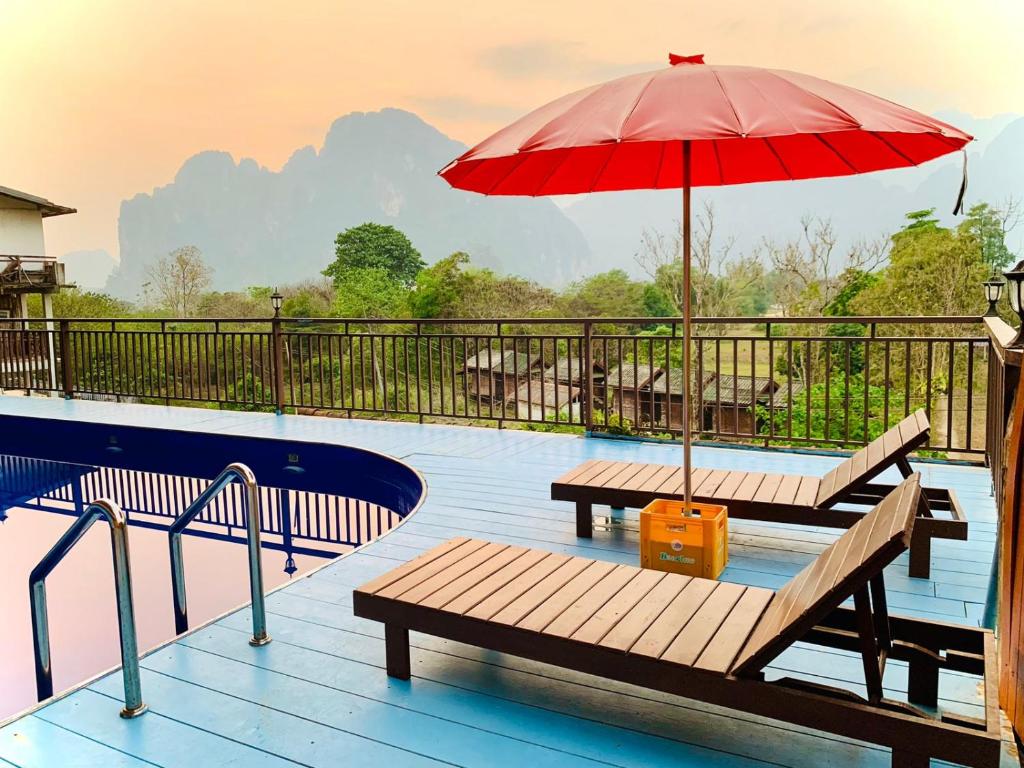 万荣Happy Riverview Hotel的一个带两个长椅和红色遮阳伞的游泳池