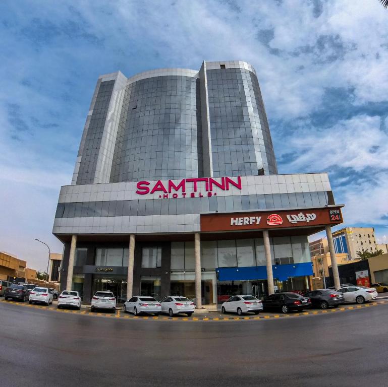 利雅德Samt Inn Hotel的一座大型建筑,前面有汽车停放