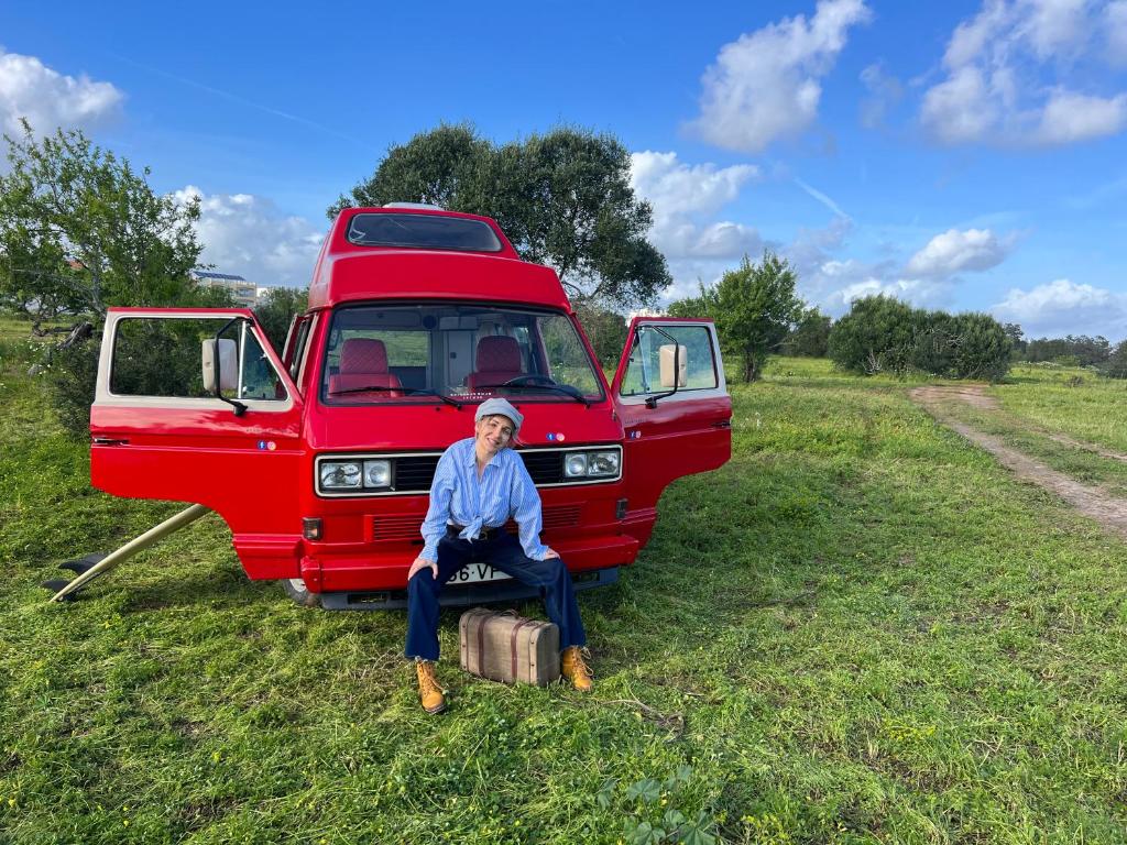 波尔蒂芒Rent a Blue Classics' s Campervan for your Road trip in Portimao -VOLKSWAGEN T3的坐在红色面包车前手提箱上的女人