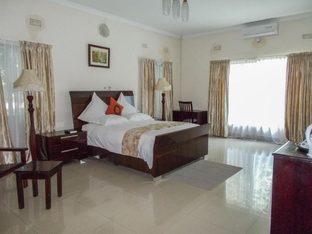 卢萨卡Waterfalls hotel (Lusaka)的一间卧室配有一张床、一张书桌和一个窗户。