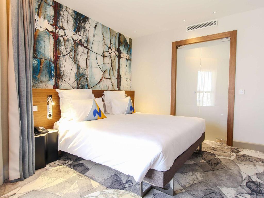突尼斯Novotel Tunis Lac的卧室配有一张白色大床,墙上挂有绘画作品