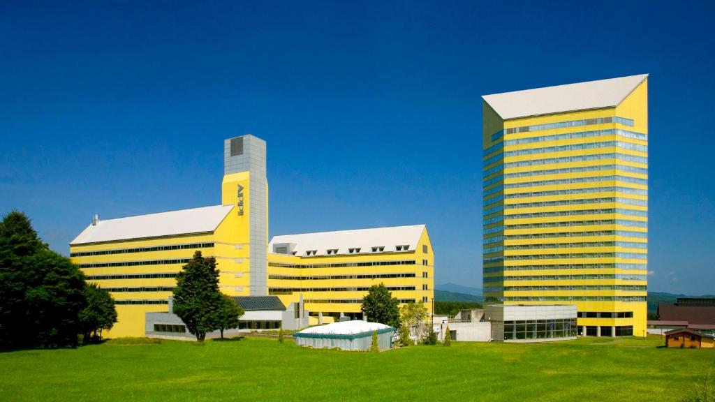 八幡平市ANA Crowne Plaza Resort Appi Kogen, an IHG Hotel的前面有3座高大的黄色建筑,有绿地