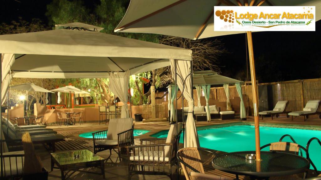 圣佩德罗·德·阿塔卡马Lodge Ancar Atacama的一个带桌椅和遮阳伞的游泳池