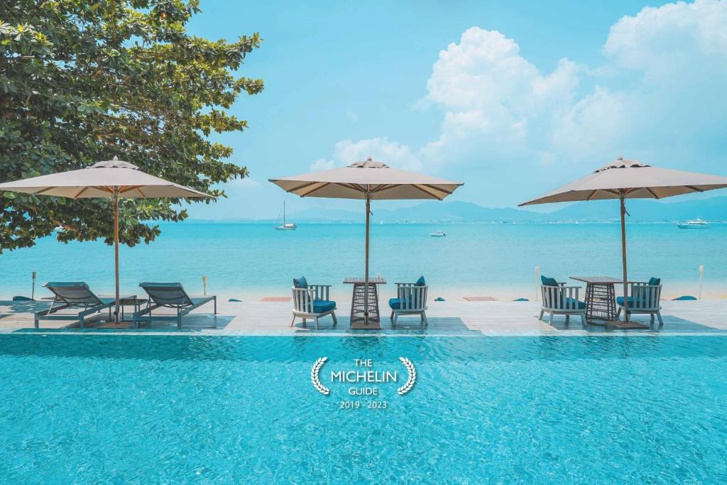 攀瓦海滩My Beach Resort Phuket的毗邻大海的带椅子和遮阳伞的游泳池