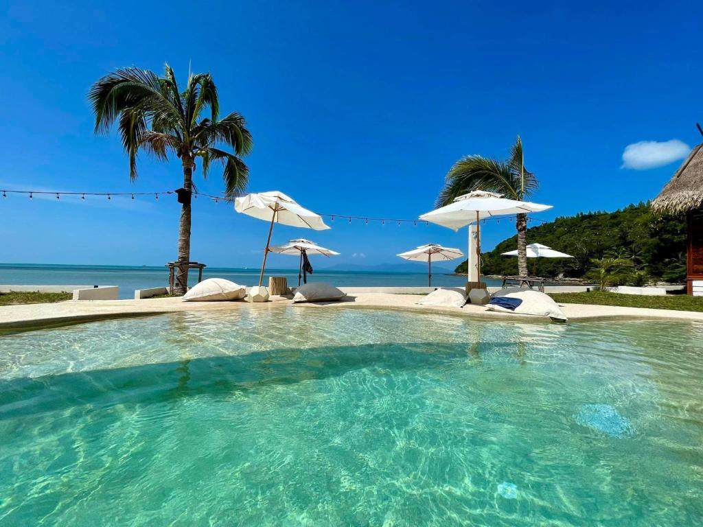 苏梅岛Le Shelby Samui Beach Resort Cottage的一个带遮阳伞和海洋的大型游泳池