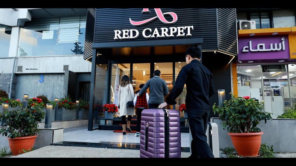 安曼Red Carpet Suites的三人站在红地毯店外面,手提紫色的手提箱