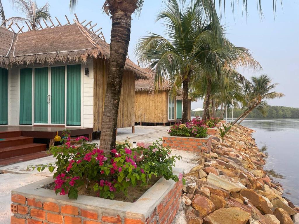Phumĭ Srê ThmeiNov Koh Kong Resort的水边有棕榈树和鲜花的房子