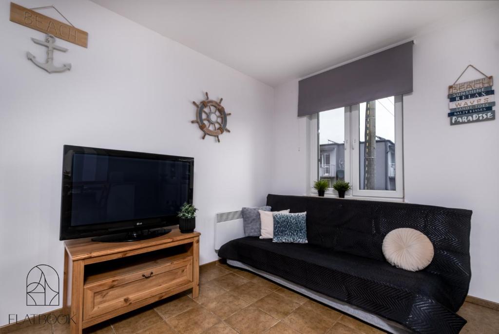 库瑞尼卡慕斯卡Flatbook Apartamenty - Krynica Morska Gdańska的客厅配有黑色沙发和平面电视。