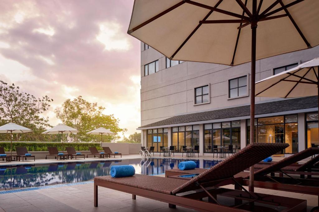 关丹AC Hotel by Marriott Kuantan的一座带椅子和遮阳伞的游泳池位于大楼旁
