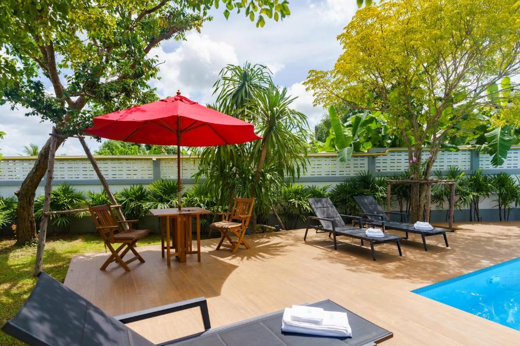 班怀雅Baan Nern Khao Resort Pattaya的庭院配有桌椅和红色遮阳伞。