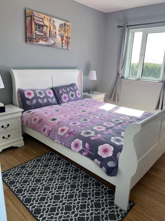科克Meelin cottage的一间卧室配有一张带紫色棉被的床和窗户。