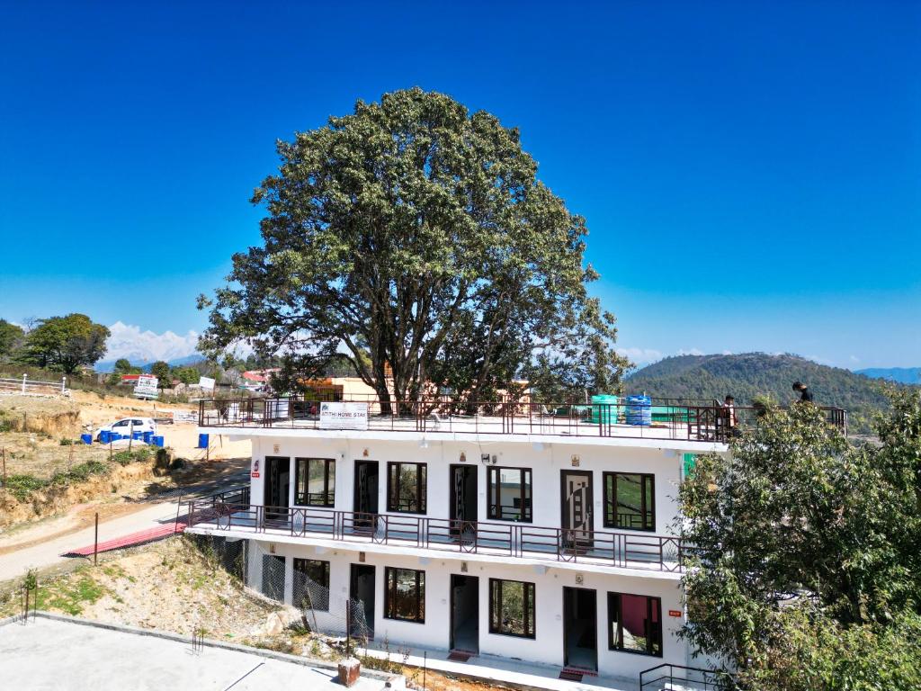 ChaukoriAtithi Home Stay - Himalayas view的一座白色的建筑,上面有一棵树