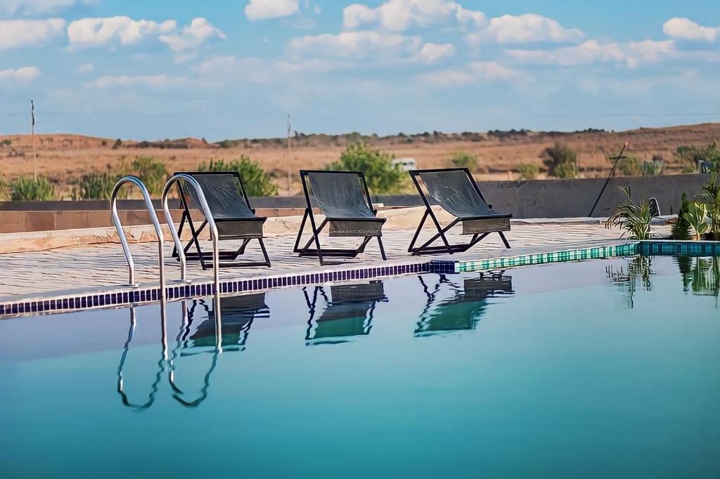斋沙默尔Jaisalmer Sam Sand Dunes Luxury Camps的游泳池旁的三把椅子