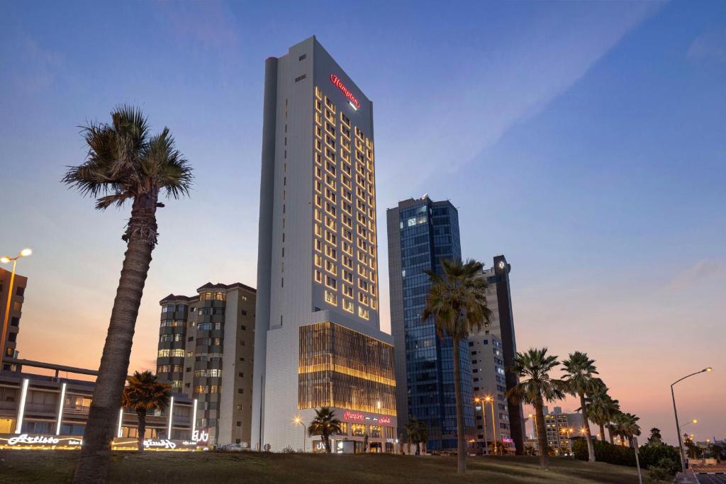 科威特Hampton By Hilton Kuwait Salmiya的一座高大的建筑,前面有棕榈树