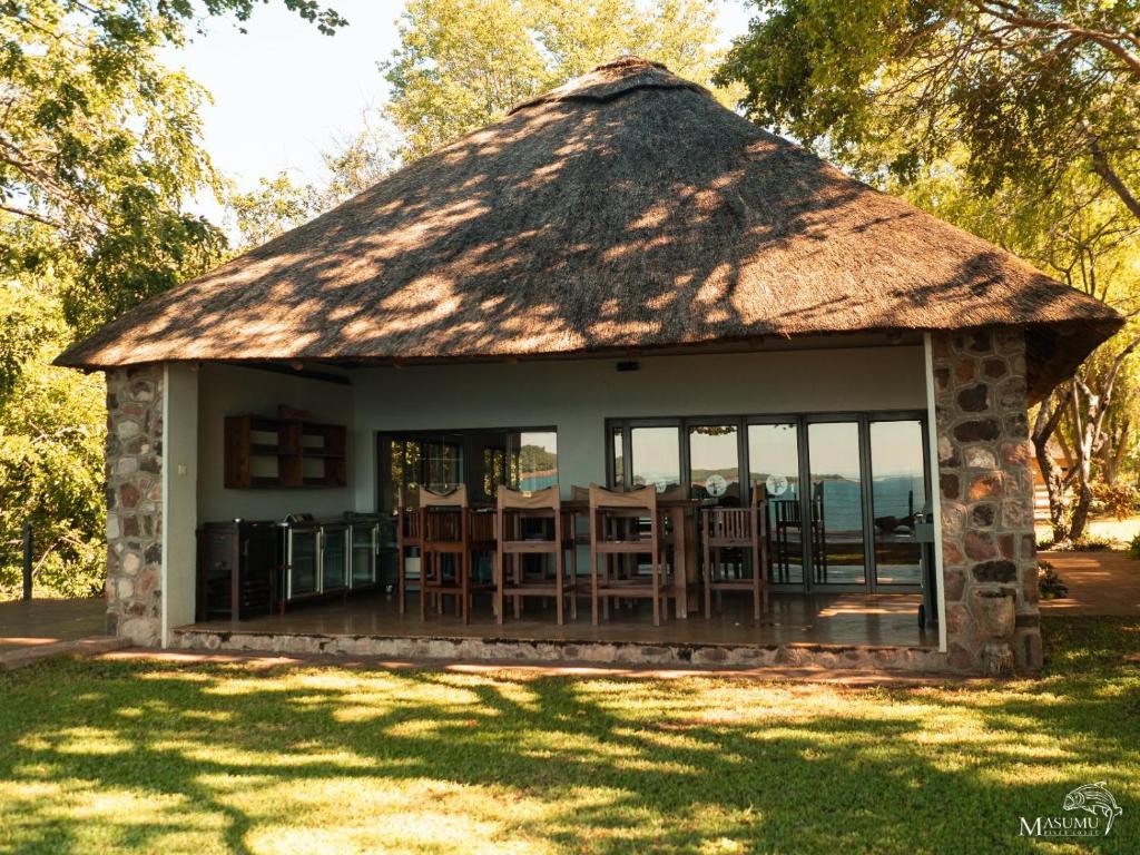BingaMasumu River Lodge的小屋设有茅草屋顶,配有桌椅