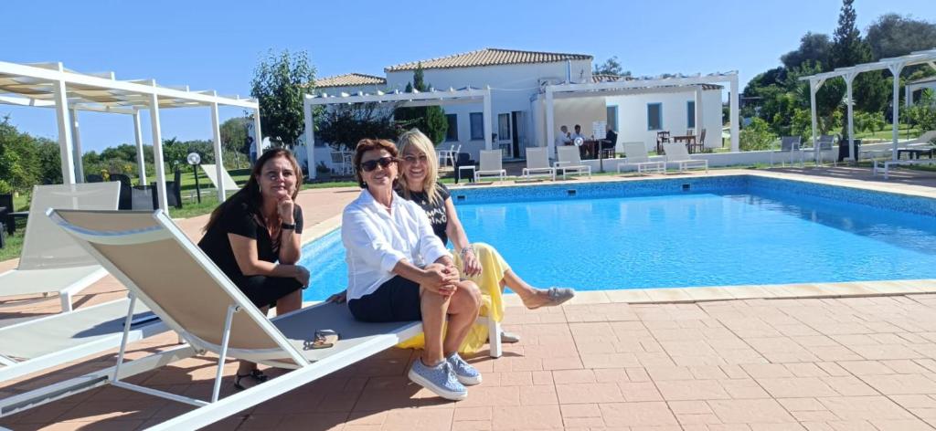 巴里萨尔多拜亚塞酒店的三个女人坐在游泳池旁的长椅上