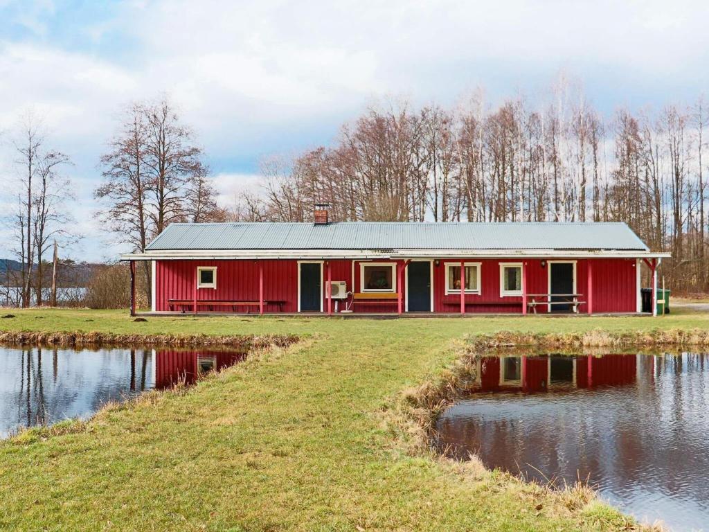 VåxtorpHoliday home VÅXTORP II的水体旁田野上的红色房子