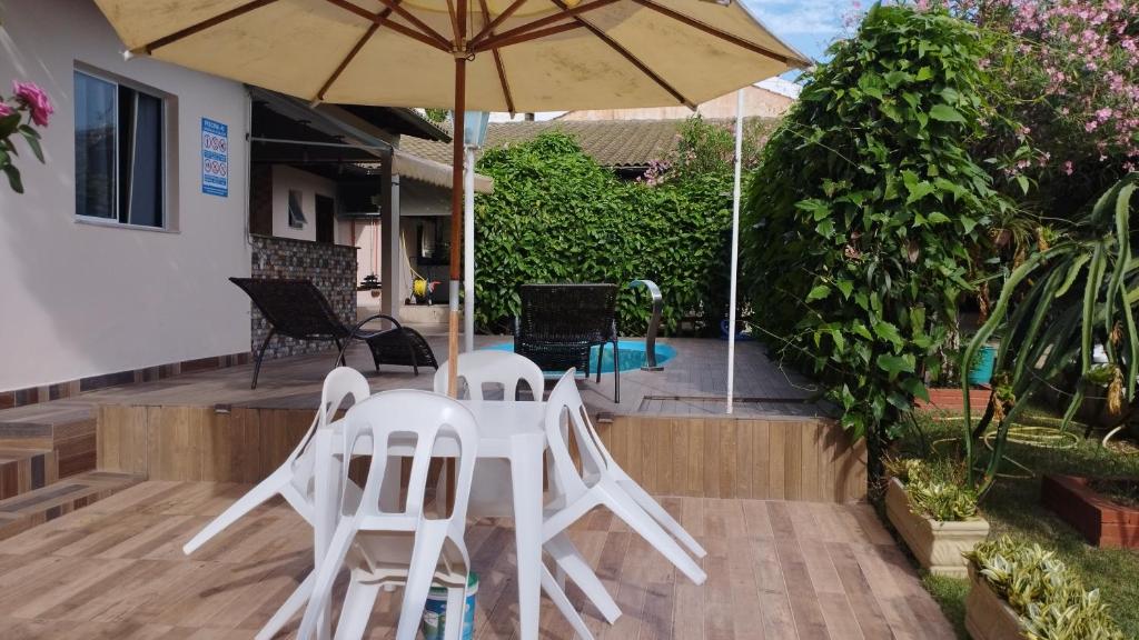 瓜拉派瑞Casa c/ Piscina e Área Gourmet, 5 min da praia.的庭院里设有两把白色椅子和一把遮阳伞