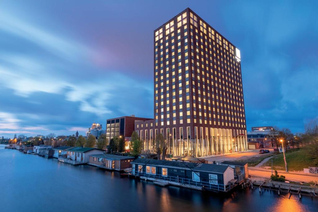 阿姆斯特丹Leonardo Royal Hotel Amsterdam的一座高大的建筑,位于河边,有一座建筑