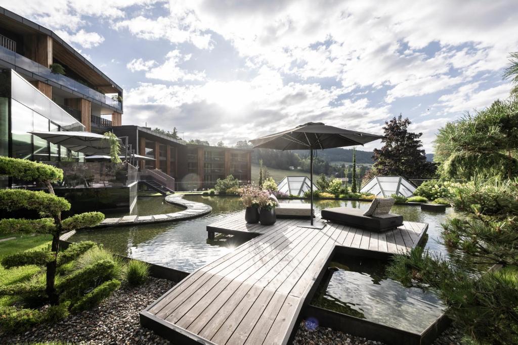 阿维兰奥Alpine Spa Resort Viktoria的一个带遮阳伞和池塘的木制甲板