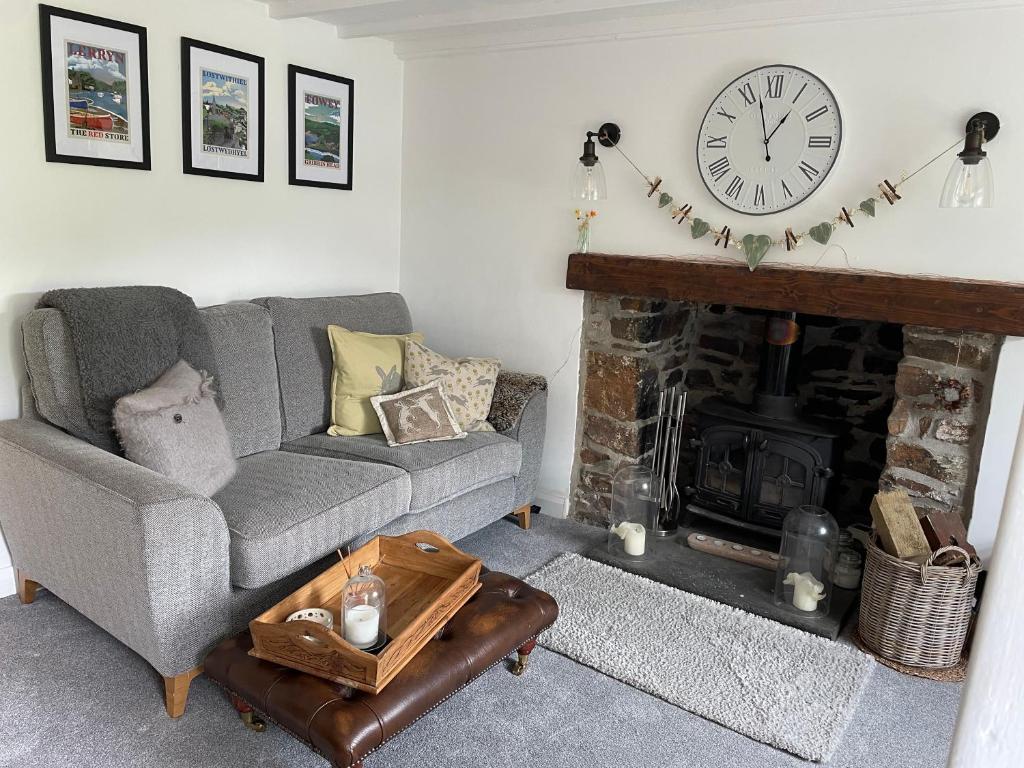 洛斯特威希尔Tiny romantic cottage for two.的客厅配有沙发和带时钟的壁炉