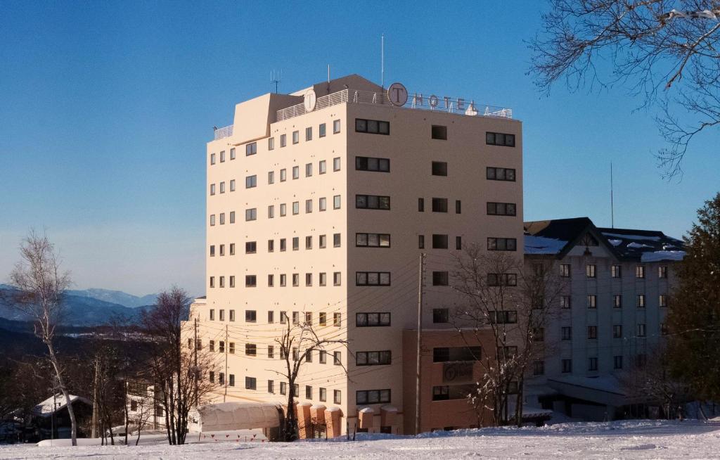 ShimotakaiT Hotel Ryuoo的一座高大的白色建筑,地面上积雪