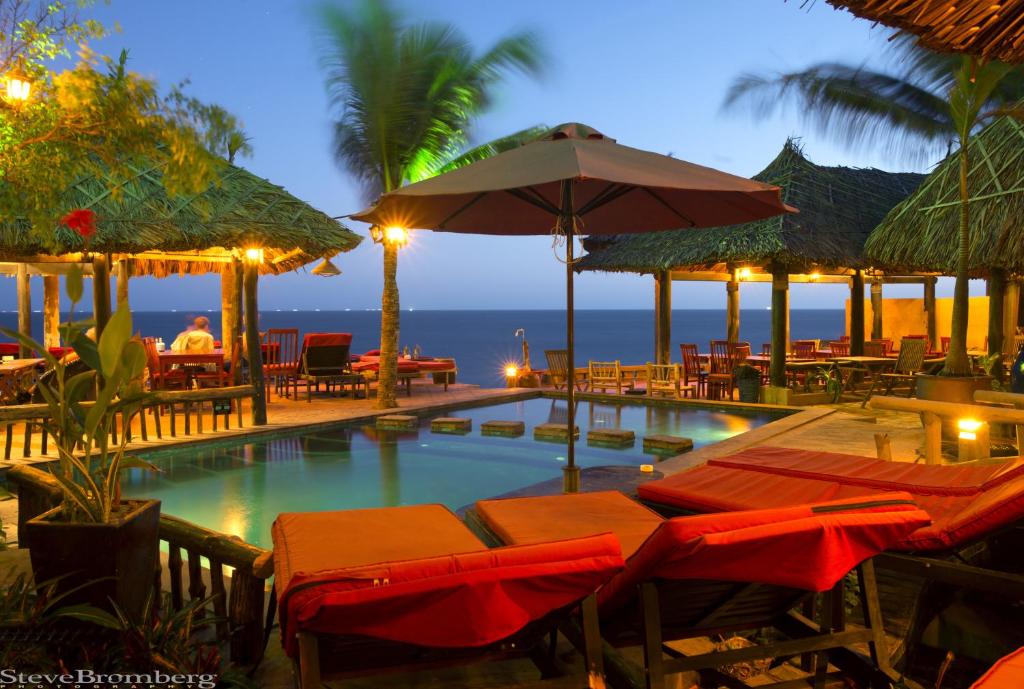 美奈乔伊咖啡厅&花园度假酒店的一个带椅子和遮阳伞的游泳池以及大海