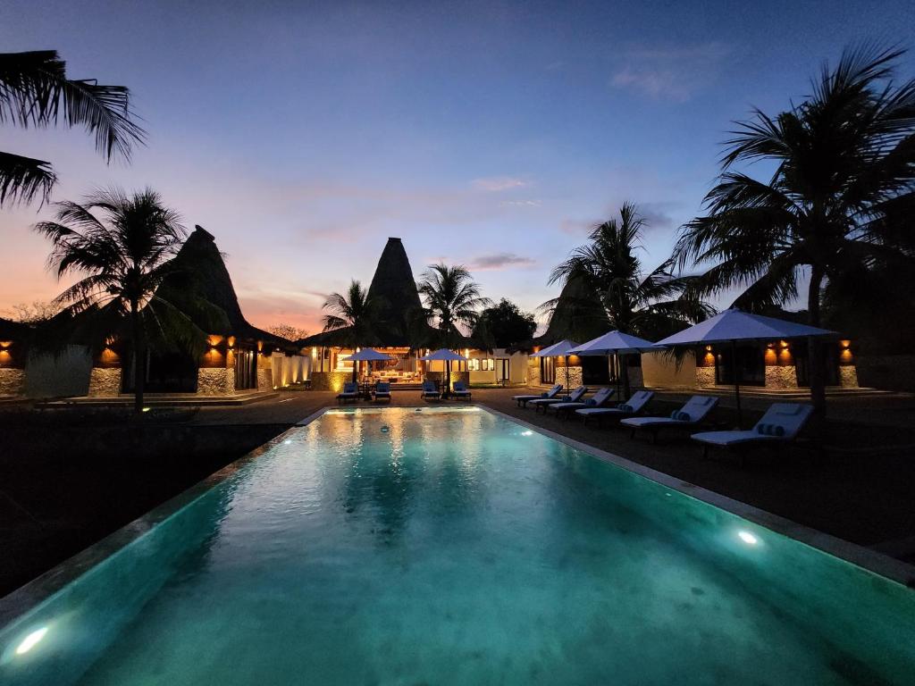 MaujawaKANDORA Luxury villas的游泳池在晚上提供椅子和遮阳伞