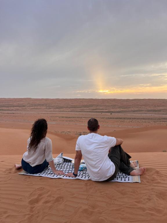 BadīyahMarbella bungalows desert的坐在沙漠中毯子上的男人和女人
