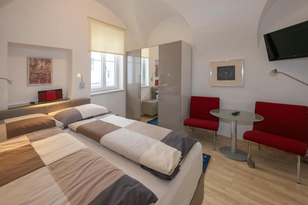克拉根福Apartments Alter Platz的一间卧室配有两张床、一张桌子和红色椅子。