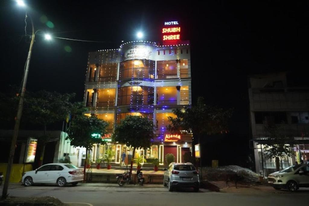 比拉斯布尔Hotel Shubh Shree Bilaspur的夜间有灯的建筑,汽车停在前面