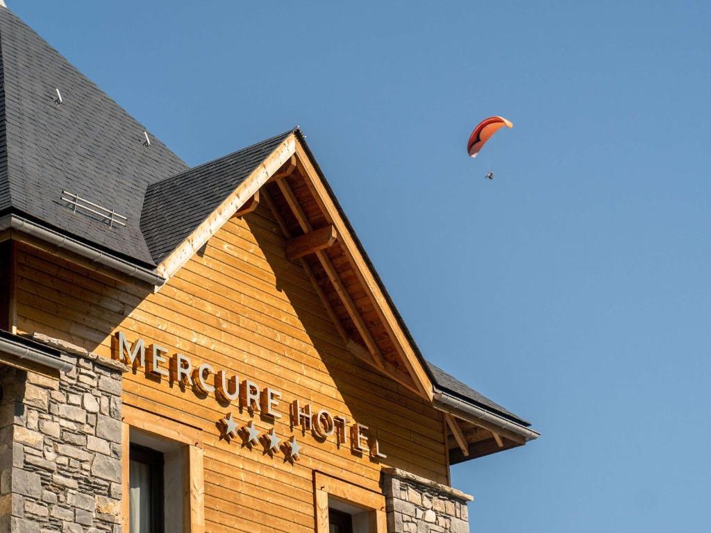 卢登维耶尔Mercure Peyragudes Loudenvielle Pyrénées的风筝飞过一座建筑物,上面有标志