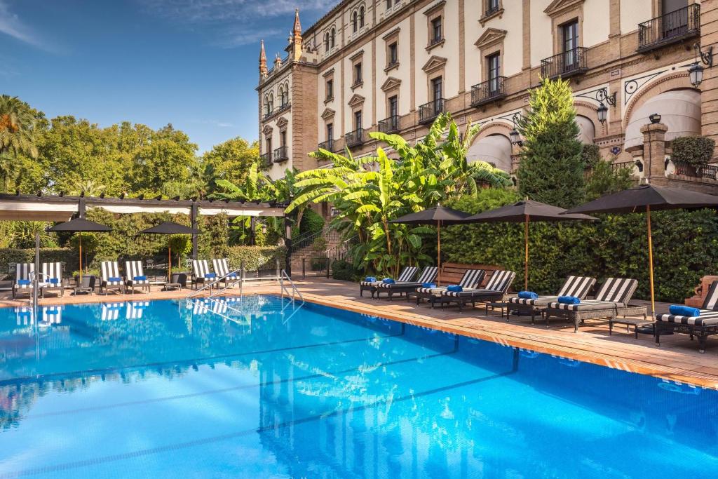 塞维利亚Hotel Alfonso XIII, a Luxury Collection Hotel, Seville的一座带椅子和遮阳伞的游泳池位于一座建筑旁边