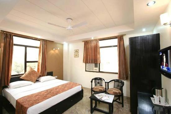 新德里Hotel Jeniffer Inn的一间卧室设有一张床、一台电视和两个窗户。