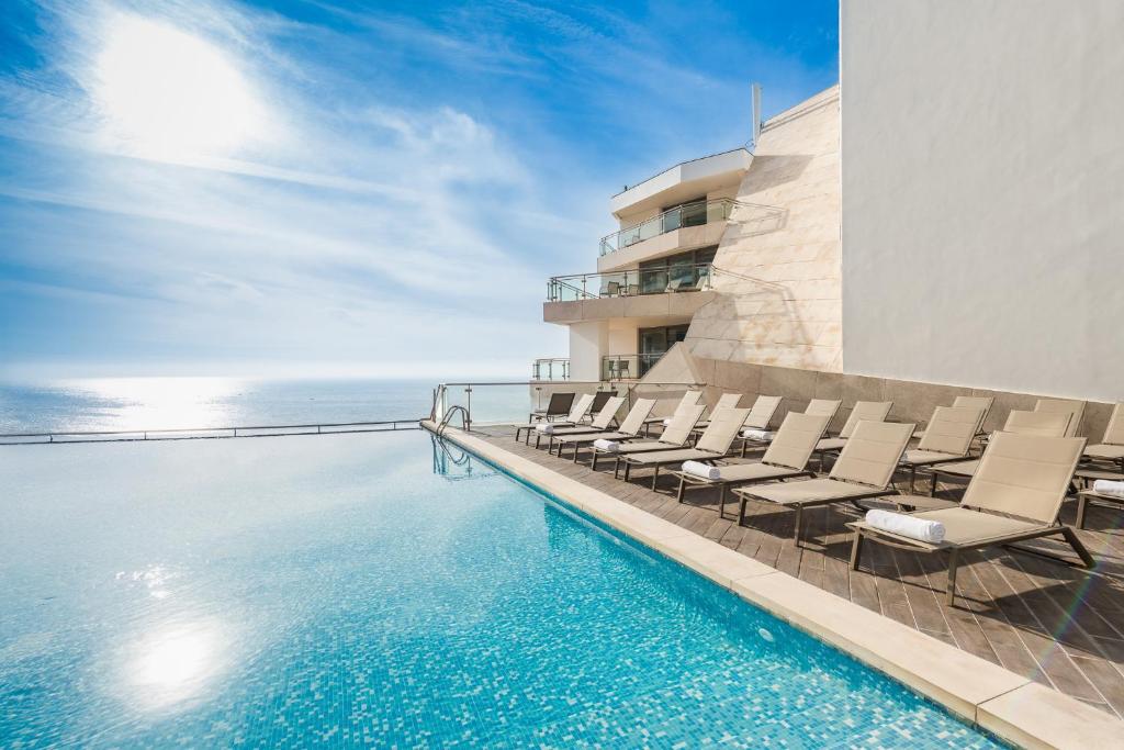 塞辛布拉Sesimbra Oceanfront Hotel的一个带椅子的游泳池,背景是大海