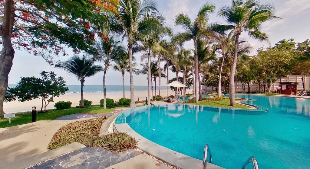 华欣2BR Beachfront Condo in central HuaHin, Baan Saen Ploen的棕榈树和海滩的游泳池