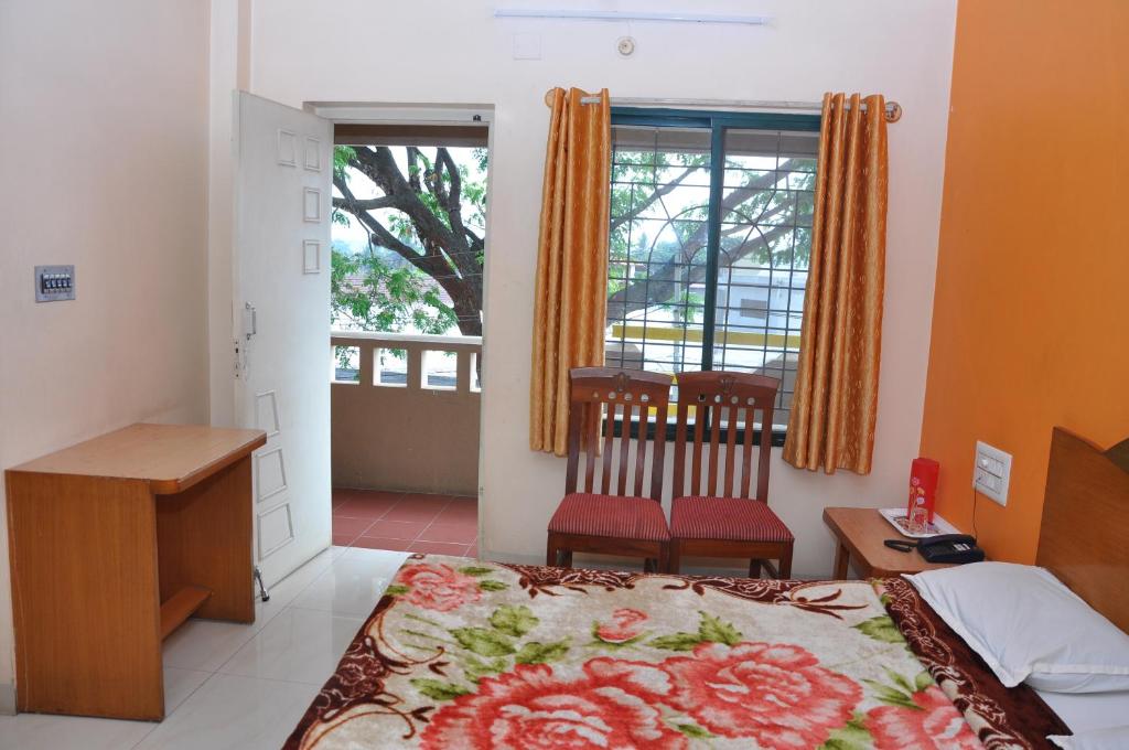 库斯哈尔纳加尔Vinayaka Deluxe Lodge的一间卧室配有一张床、一张书桌和一个窗户。