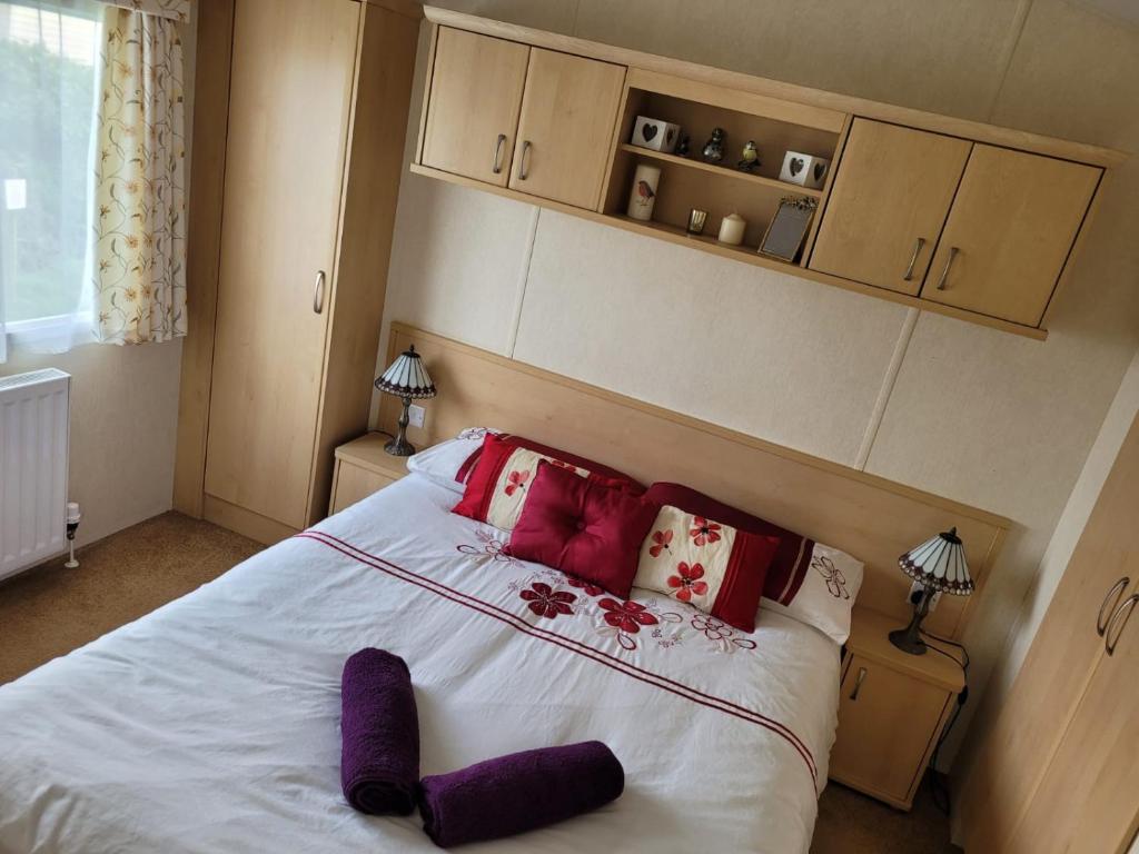 LlwyngwrilCosy caravan Sunbeach的卧室配有带红色枕头的大型白色床