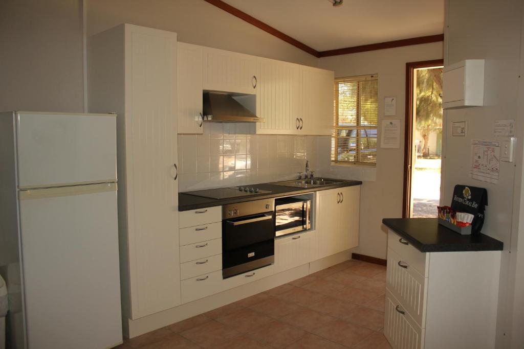 珊瑚湾珊瑚湾宁乐酒店 - 湾景的厨房配有白色橱柜、水槽和冰箱。