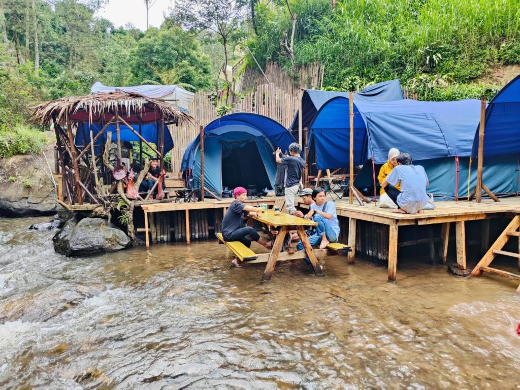 万隆Camping Pines singkur reverside的一群人坐在河里桌子上,有帐篷
