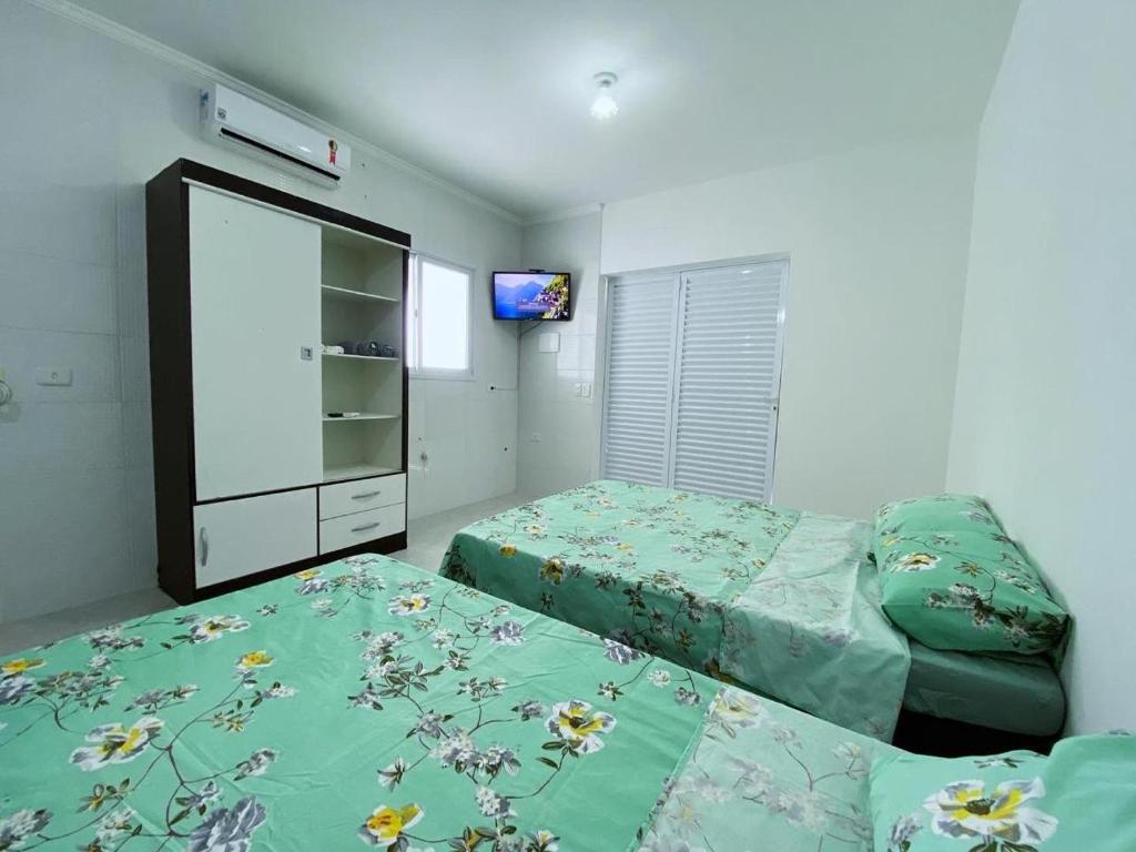 佩鲁伊比Pousada e Espaco AURORA Peruibe的一间卧室设有两张床,墙上配有电视。