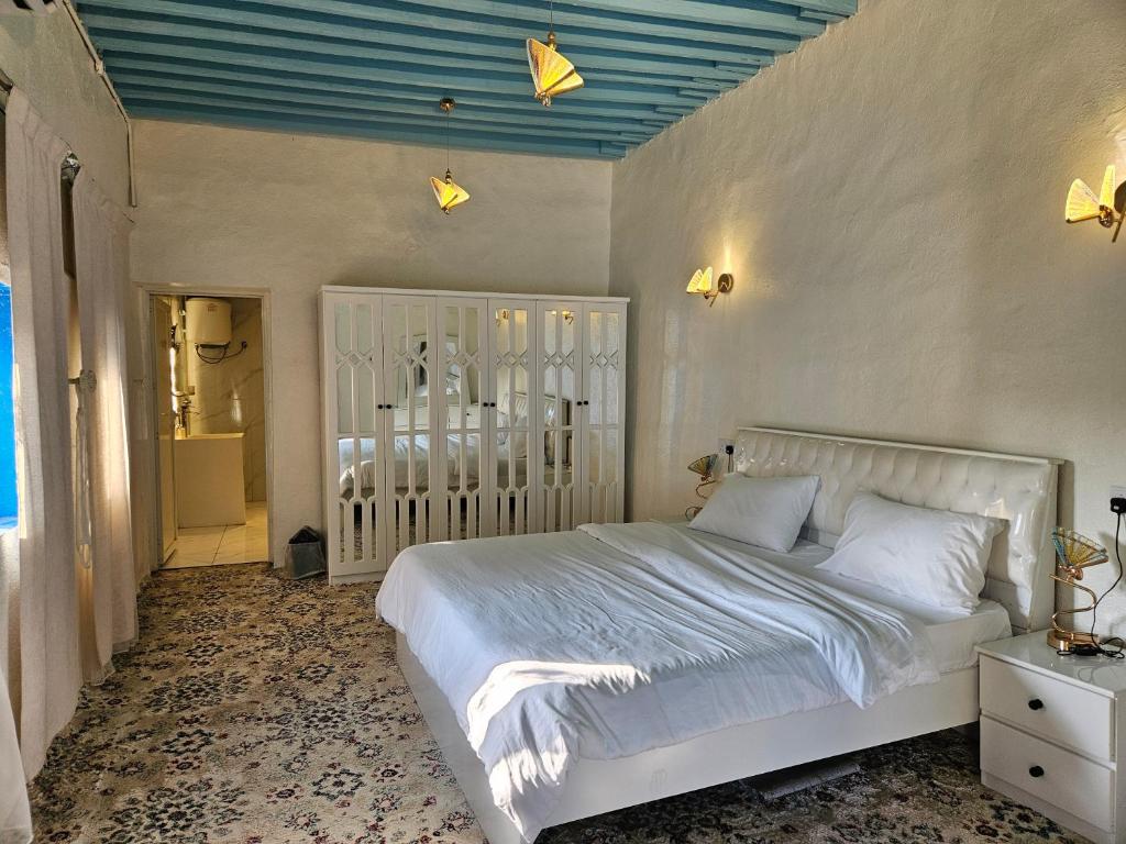 Ḩajlahمنزل حجري بحديقتين的卧室配有白色的床和蓝色的天花板