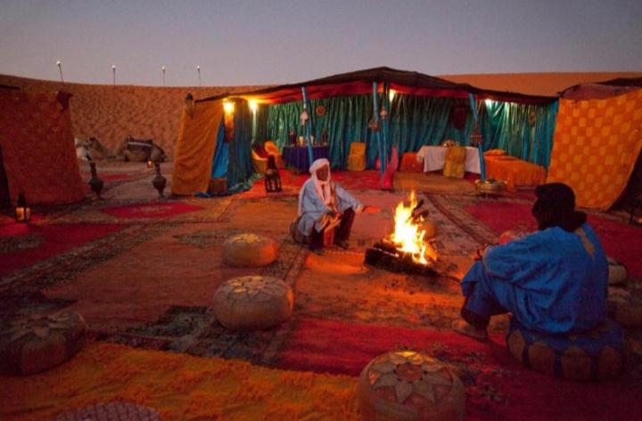 梅尔祖卡Desert Berber Camp的两个人坐在帐篷里,围着火