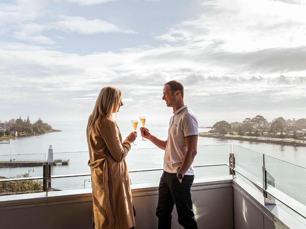 德文港Novotel Devonport的一名男子和一名女子在阳台上持有香槟杯
