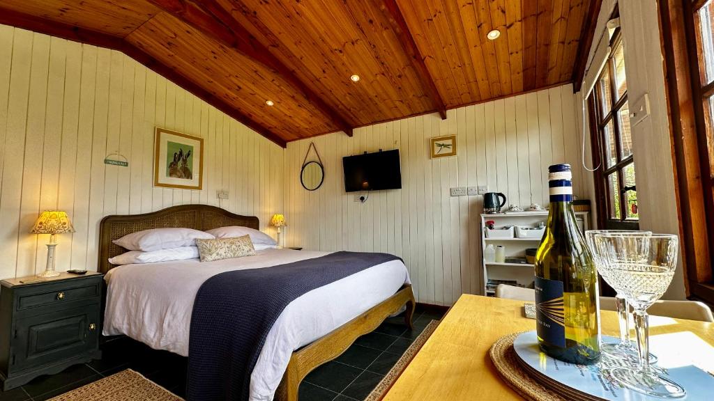 威尔汉姆The Cider Shed Bed and Breakfast的一间卧室配有一张床和一张桌子及一瓶葡萄酒