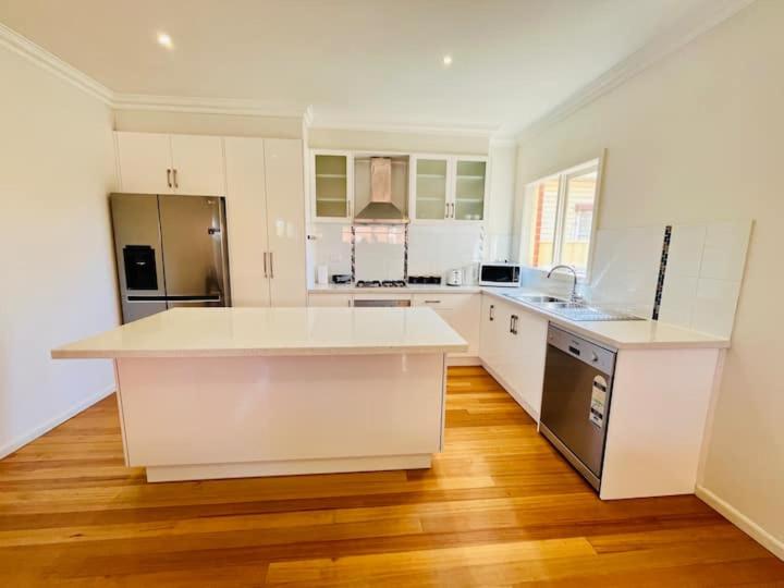 墨尔本Townhouse Near The World’s Coolest High st in 2024的一间铺有木地板的大厨房,配有白色的橱柜