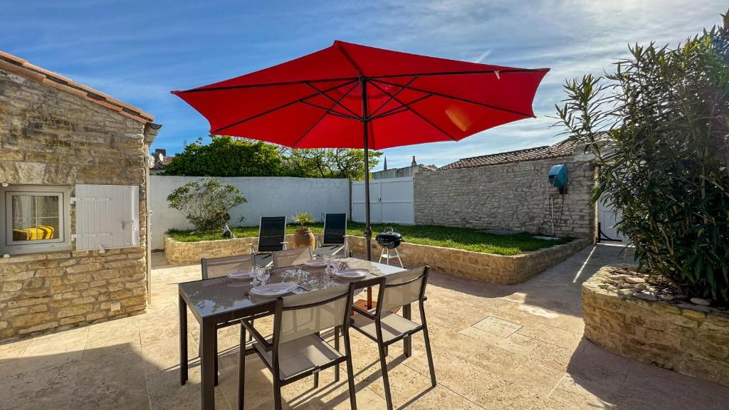 阿尔桑雷Dans le centre du village d'ARS EN RE, charmante villa bien décorée的露台上的一张桌子和一把红色遮阳伞